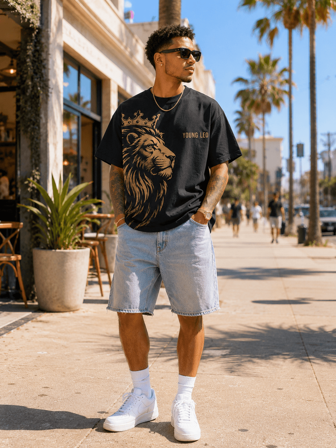 Man wearing The Becoming Tee with the crowned lion front print, on a palm-lined street